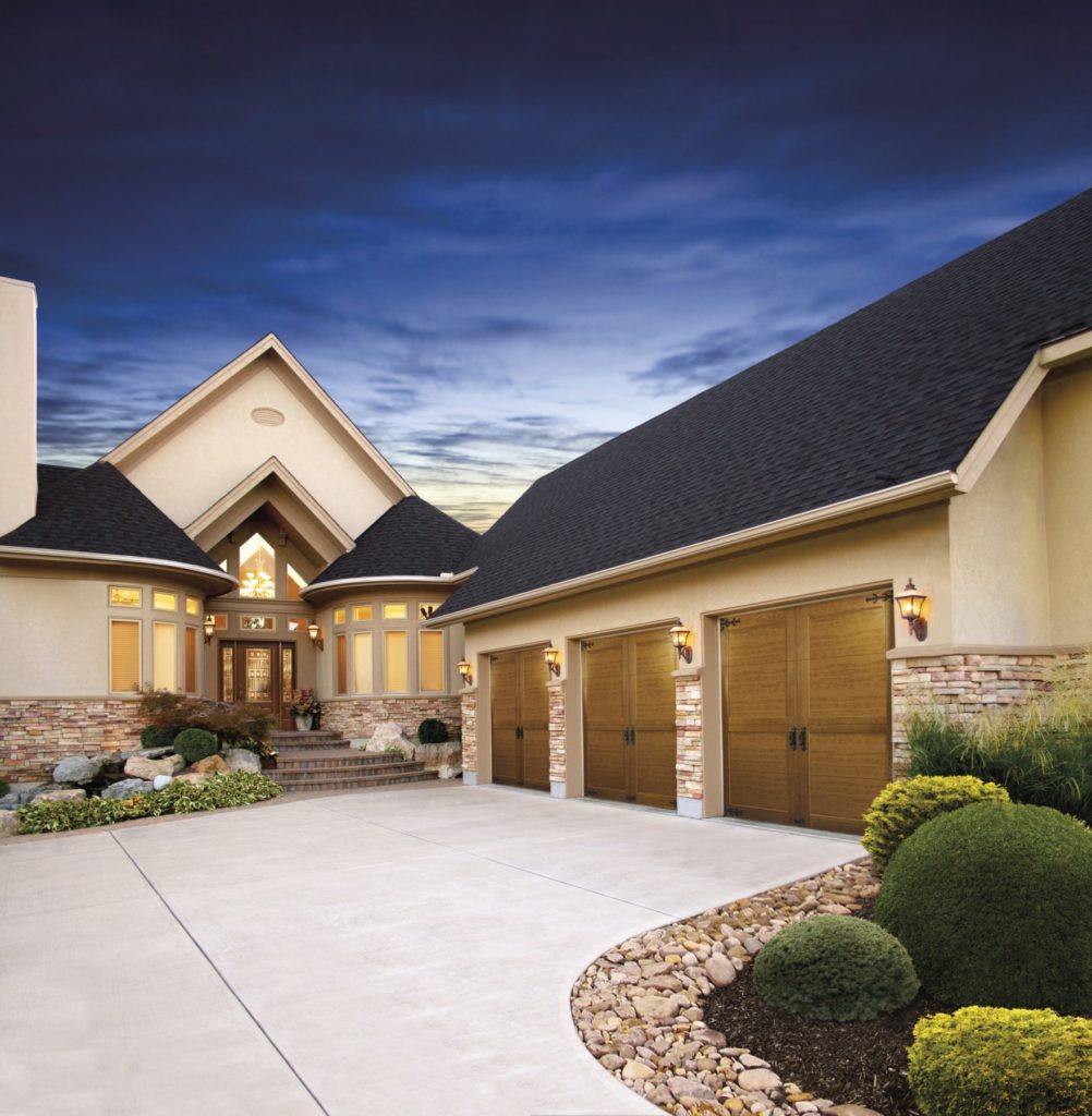 Three Clopay CANYON RIDGE® COLLECTION — ULTRA-GRAIN® Series garage doors on a home with a dark night sky